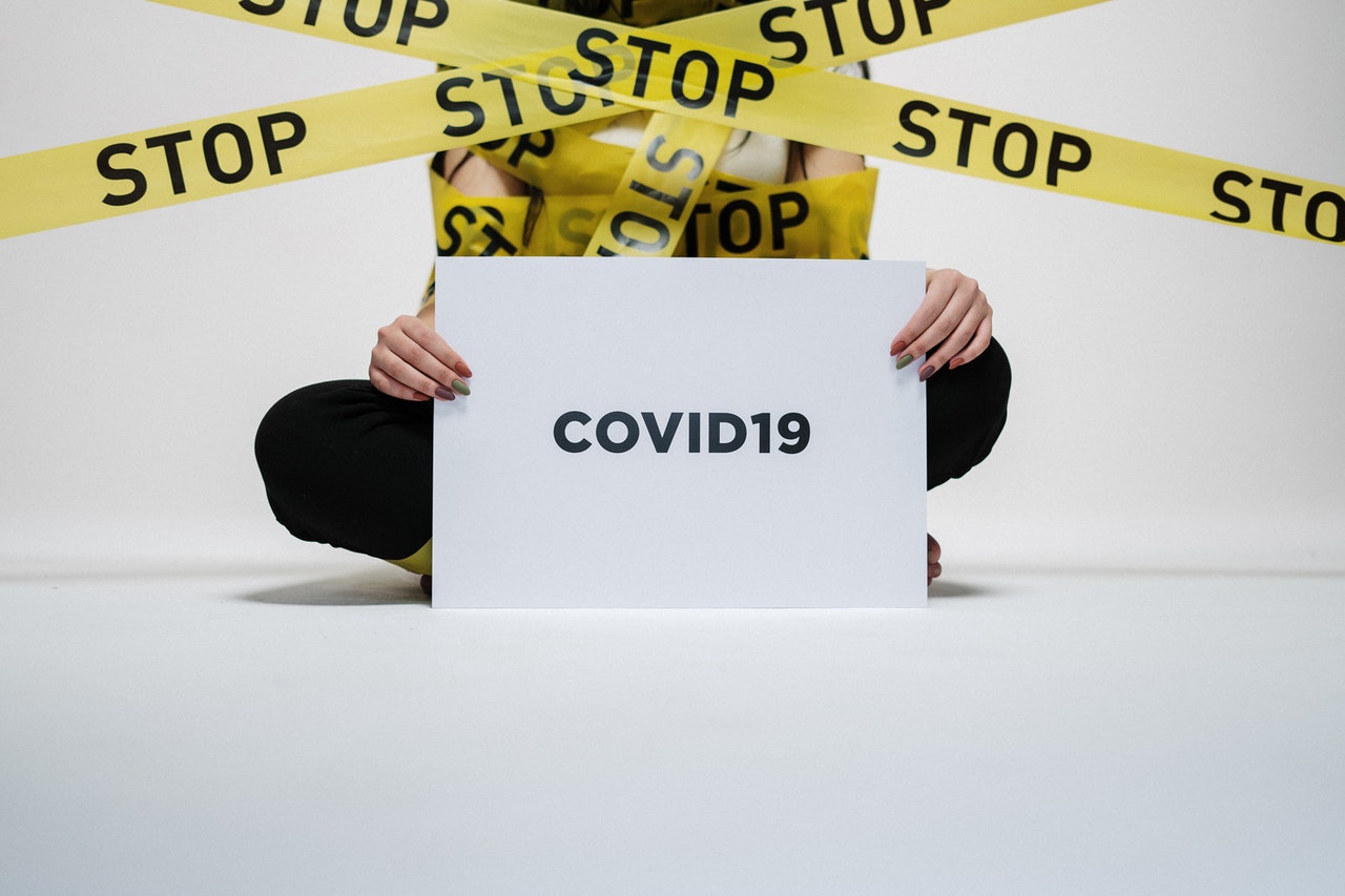 Woman is sitting with her legs crossed and is holding a paper with covid wrote on it