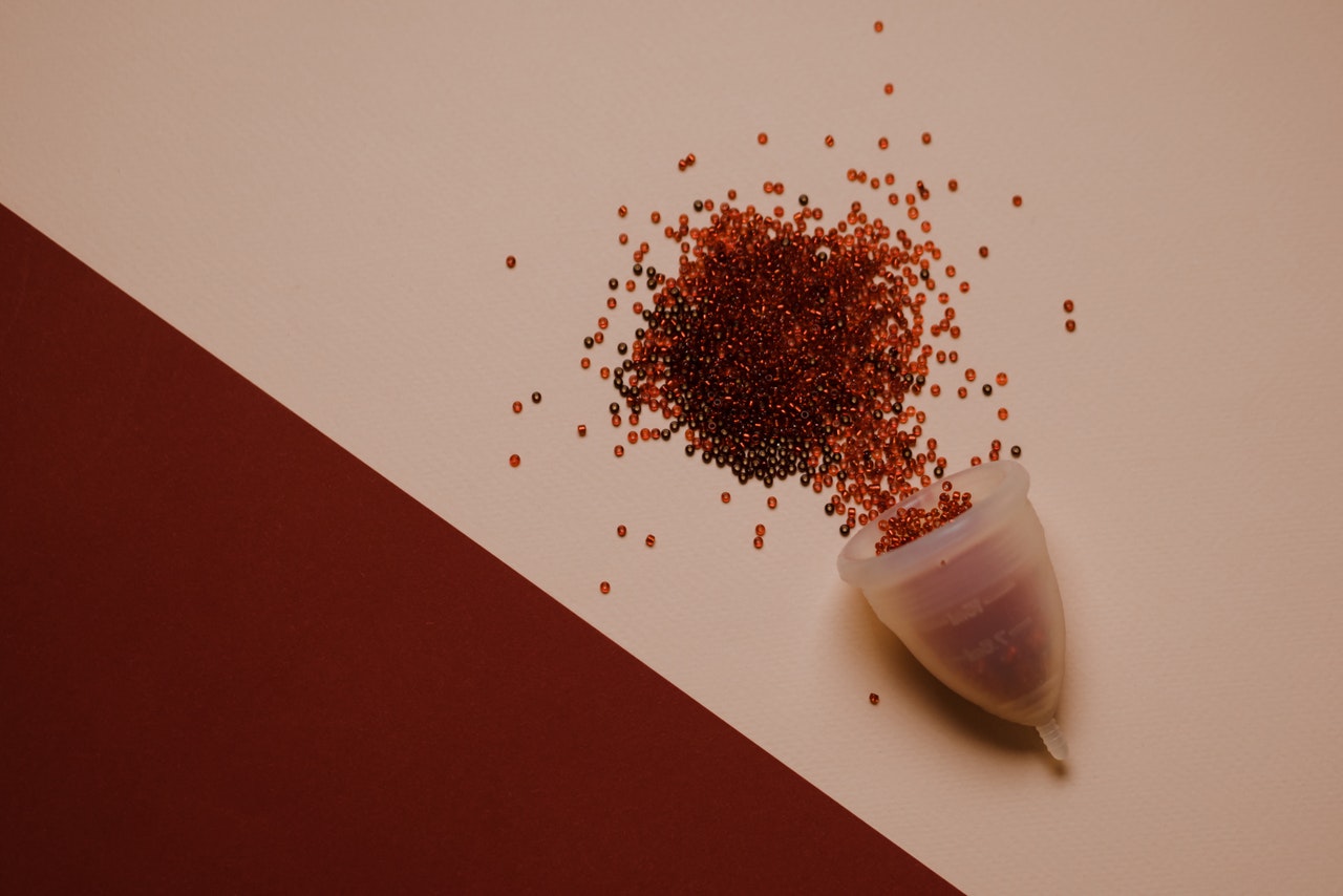 Period cup with red red beads falling out of it on table